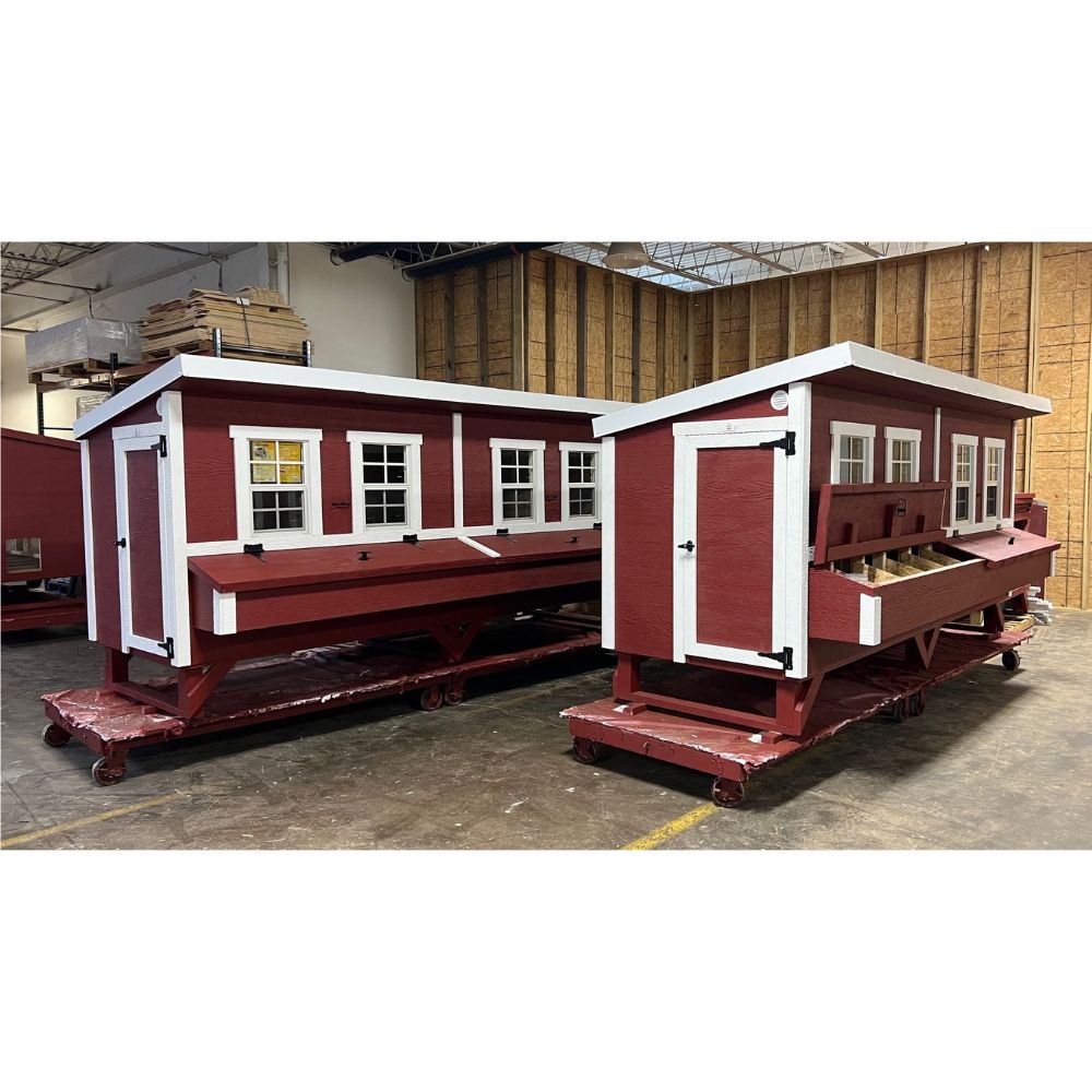 Two red and white chicken coops with four windows on pallets, fully assembled at warehouse.