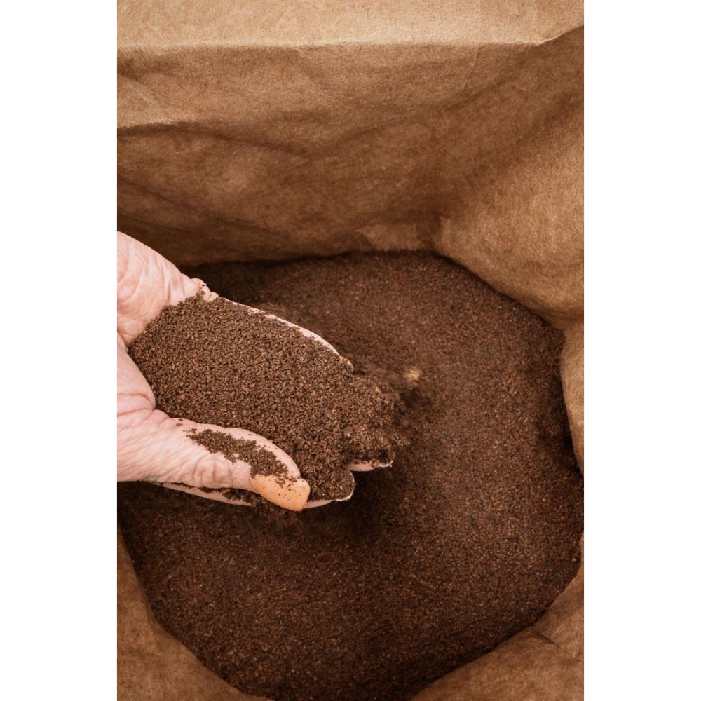 Open bag of OverEZ Coffee ground bedding with a hand lifting a handful for display.
