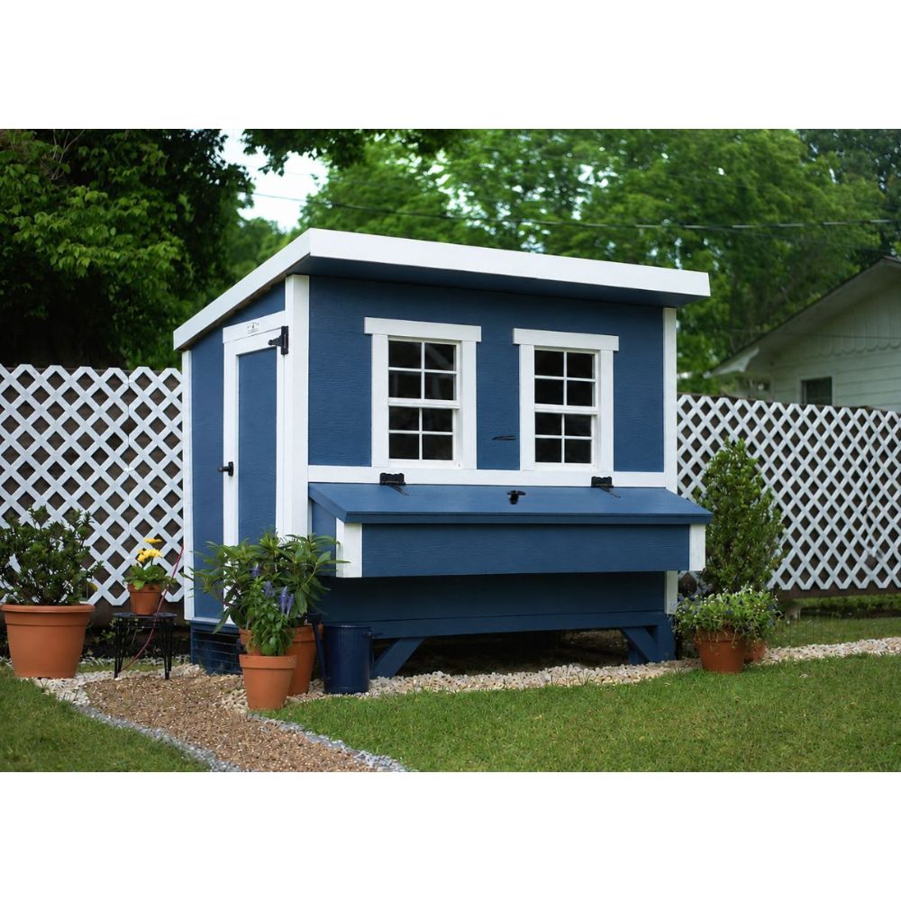 A blue and white wooden chicken coop, set in a backyard with a white lattice fence, and potted plants.