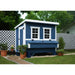 A blue and white wooden chicken coop, set in a backyard with a white lattice fence, and potted plants.