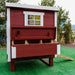 A red and white wooden chicken coop with a small window and an open lower drawer showing nesting boxes, set outdoors.