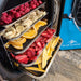 Blue Alpine freeze dryer with an open door showing five trays filled with raspberries, oranges, bananas, strawberries, and mango.