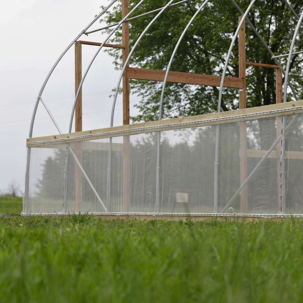 Bootstrap Farmer DIY Gothic Greenhouse during construction showing the metal arch frame, wood framing, and partially installed greenhouse covering