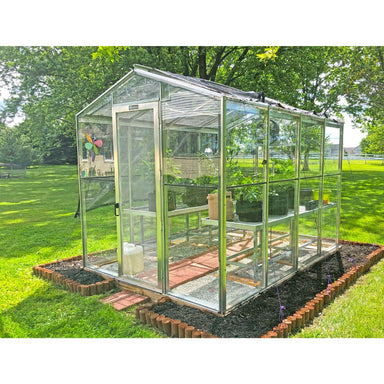 Janco Palmetto 8' x 10' glass greenhouse with aluminum frame in a backyard garden.